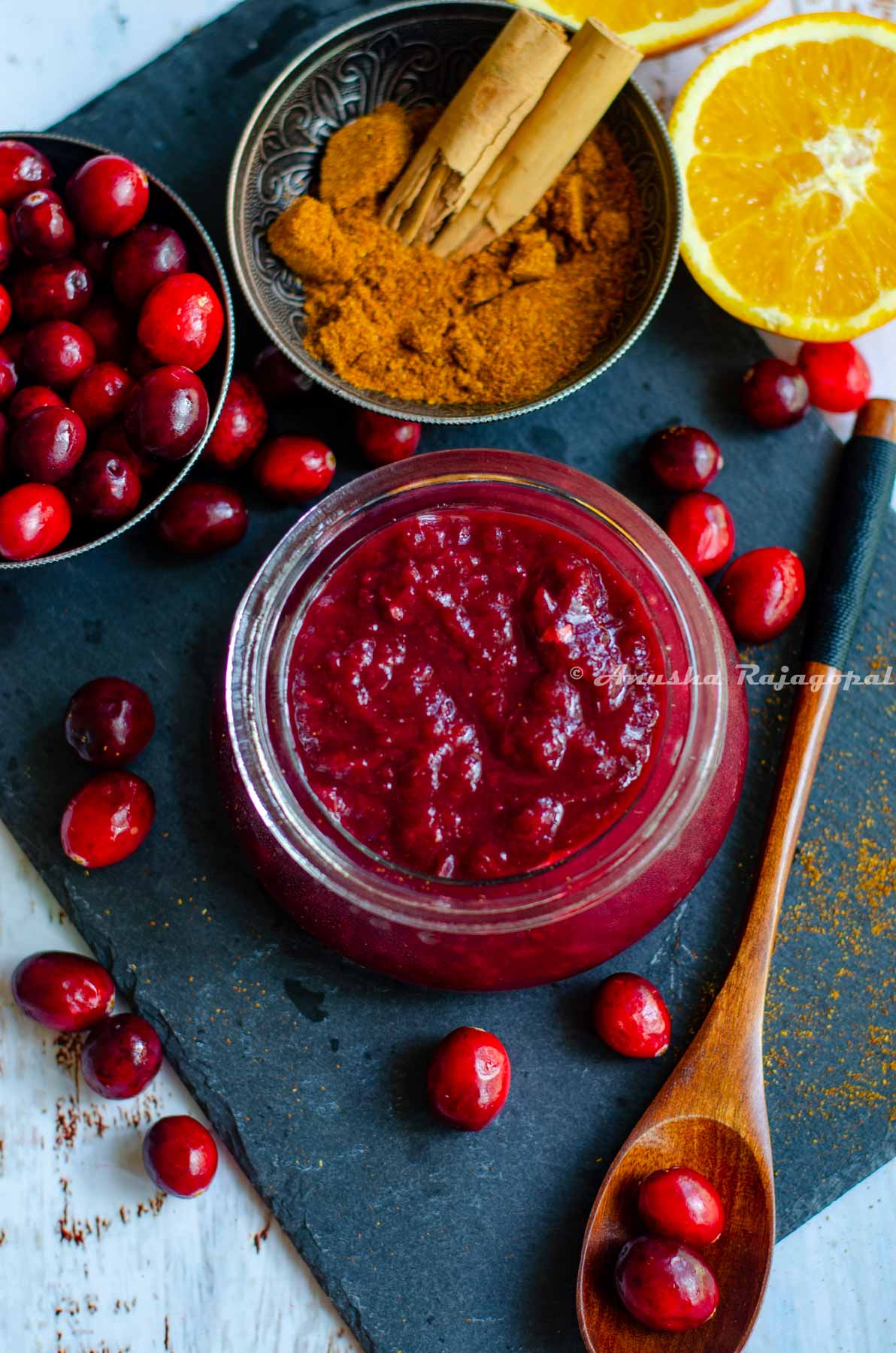 cranberry chutney made in the instant pot, served in a glass jar placed over a slate board. Cranberries, halved oranges and spices by the side.