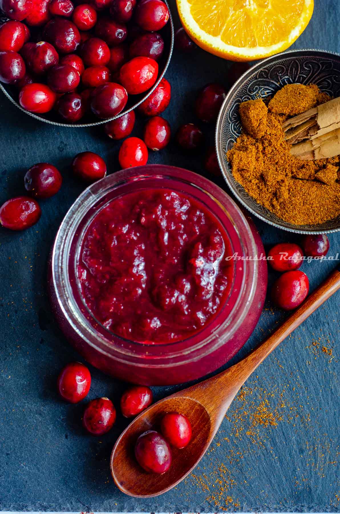 cranberry chutney made in the instant pot, served in a glass jar placed over a slate board. Cranberries, halved oranges and spices by the side.