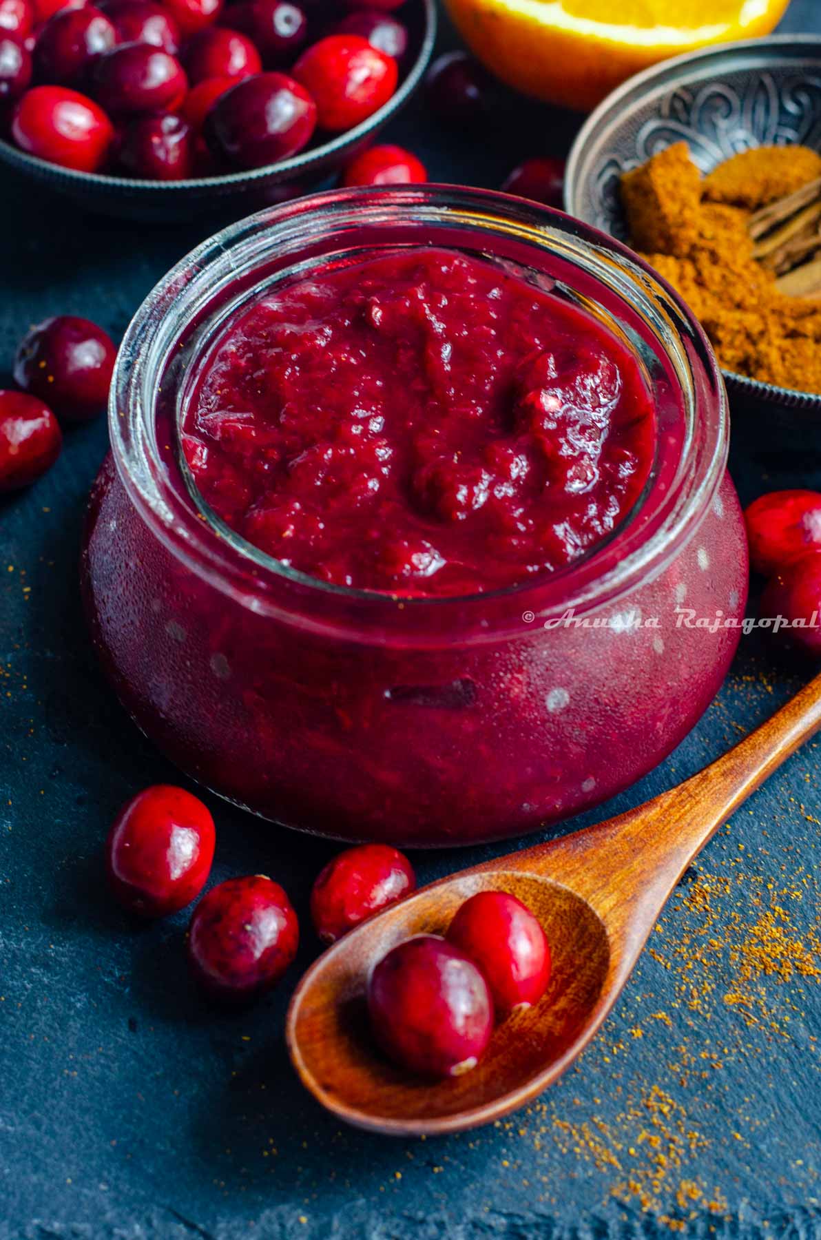 cranberry chutney made in the instant pot, served in a glass jar placed over a slate board. Cranberries, halved oranges and spices by the side.