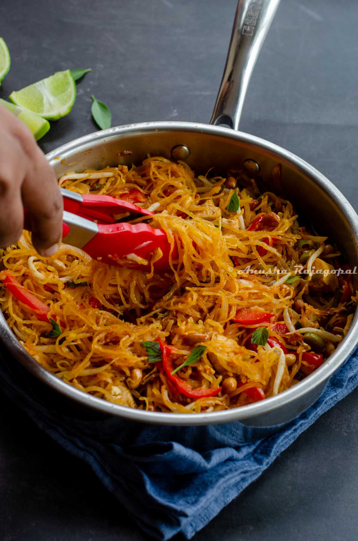 Spaghetti Squash Pad Thai in a pan being lifted out with a pair of red silicon tongs.