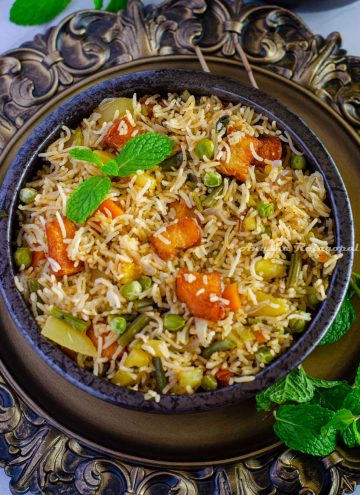 Brinji rice served in a black bowl placed over a rustic brown platter. Mint leaves by the side.