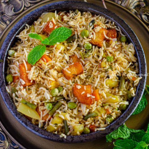Brinji rice served in a black bowl placed over a rustic brown platter. Mint leaves by the side.