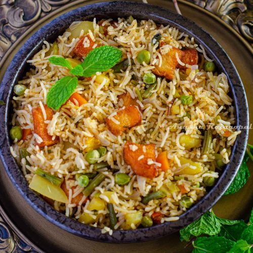 Brinji rice served in a black bowl placed over a rustic brown platter. Mint leaves by the side.