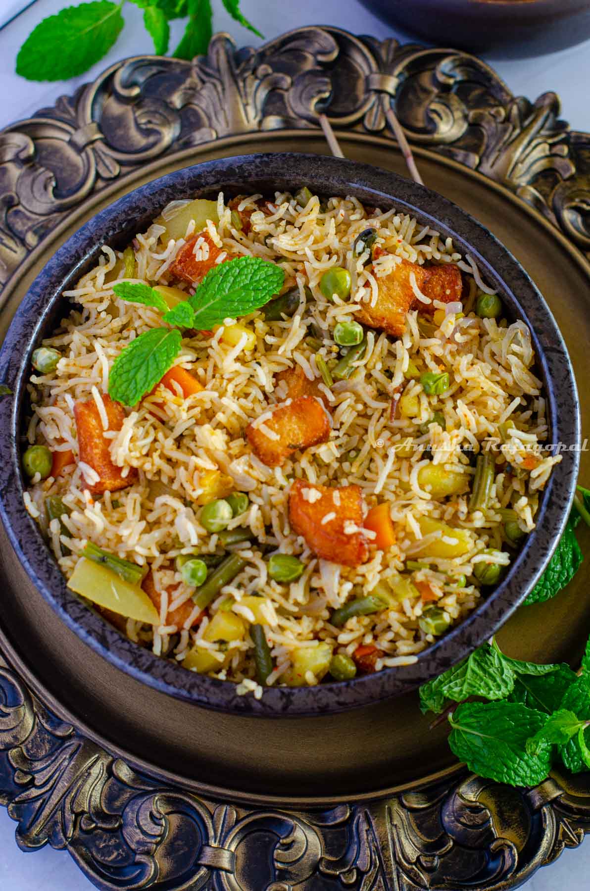 Brinji rice served in a black bowl placed over a rustic brown platter. Mint leaves by the side.