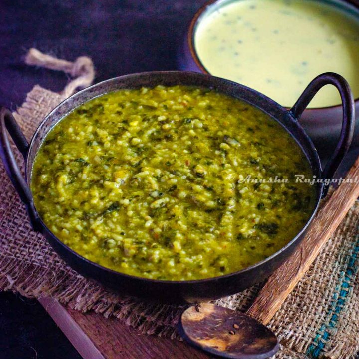 creamy palak khichdi served in an iron wok placed over a burlap mat on a wooden chopping board. Gujarati Kadhi served as an accompaniment. Wooden spoon by the side of the wok.