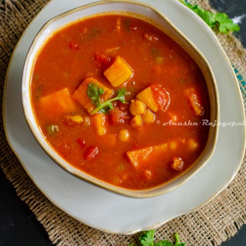 vegan sweet potato and chickpea curry serve in an asymmetrical bowl placed over a similar asymmetrical deep plate. Kept on a burlap mat against a black backrdrop. Cilantro leaves scattered by the side.