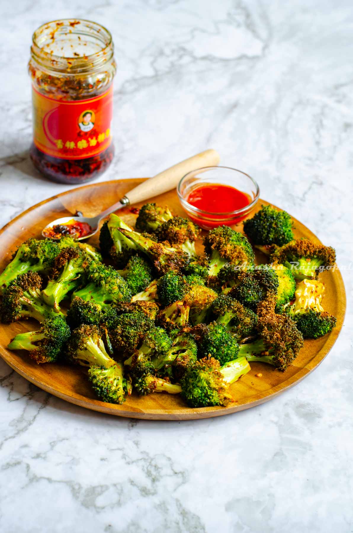 air fryer broccoli served on a wooden plate. A jar of chili crisp open at the far back of the background.