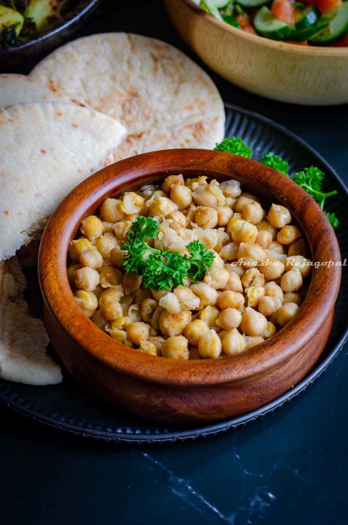 hummus balila served in a wooden bowl with pita bread and shirazi salad