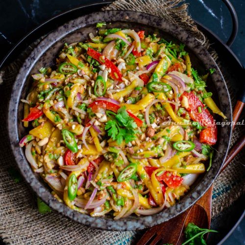 A sweet and spicy mango salad made the Thai way and served in a black shallow bowl placed over a burlap mat. Spoon and fork by the side