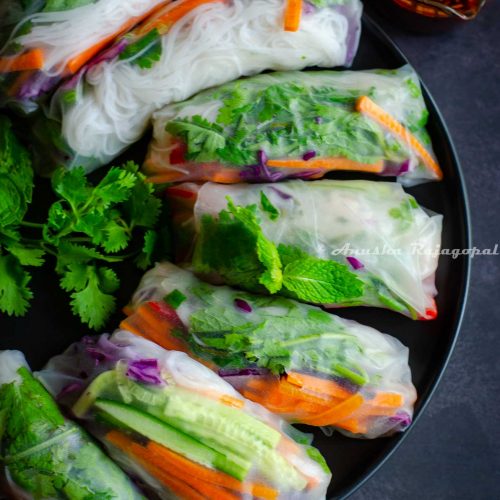 vegan summer rolls served on a plate with a spicy dipping sauce and herbs