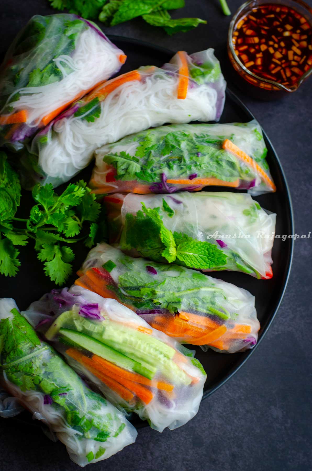 vegan summer rolls served on a plate with a spicy dipping sauce and herbs