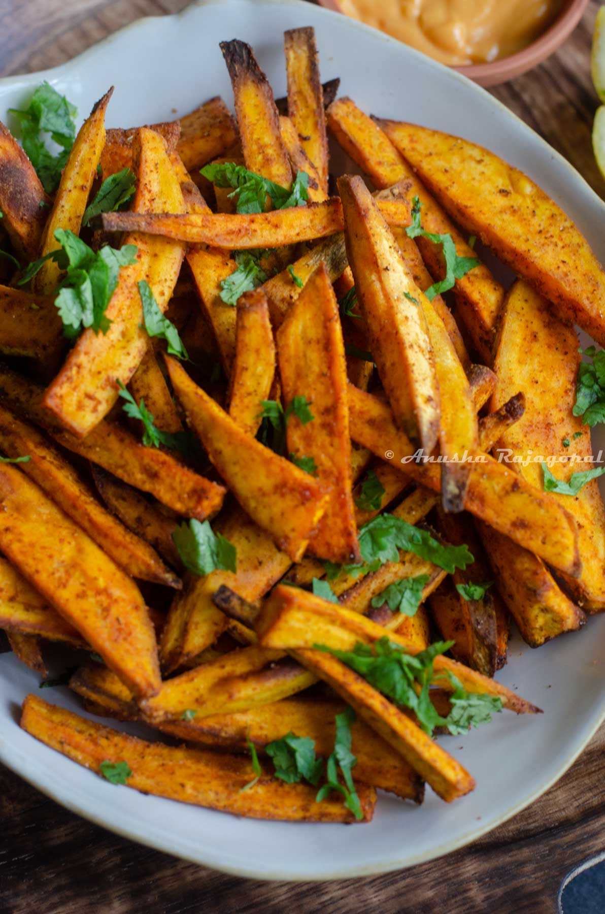 air fried sweet potato chips served in a beige irregular rimmed shallow bowl with spicy dip and lemon wedges