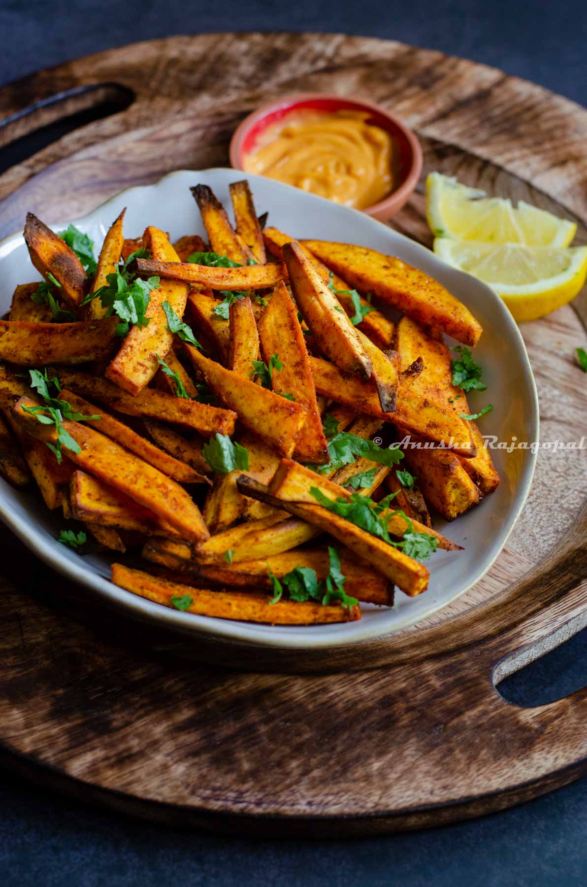 air fried sweet potato chips served in a beige irregular rimmed shallow bowl with spicy dip and lemon wedges