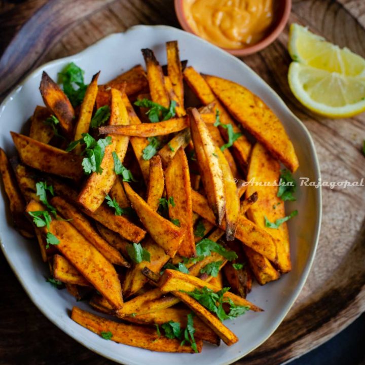 air fried sweet potato chips served in a beige irregular rimmed shallow bowl with spicy dip and lemon wedges