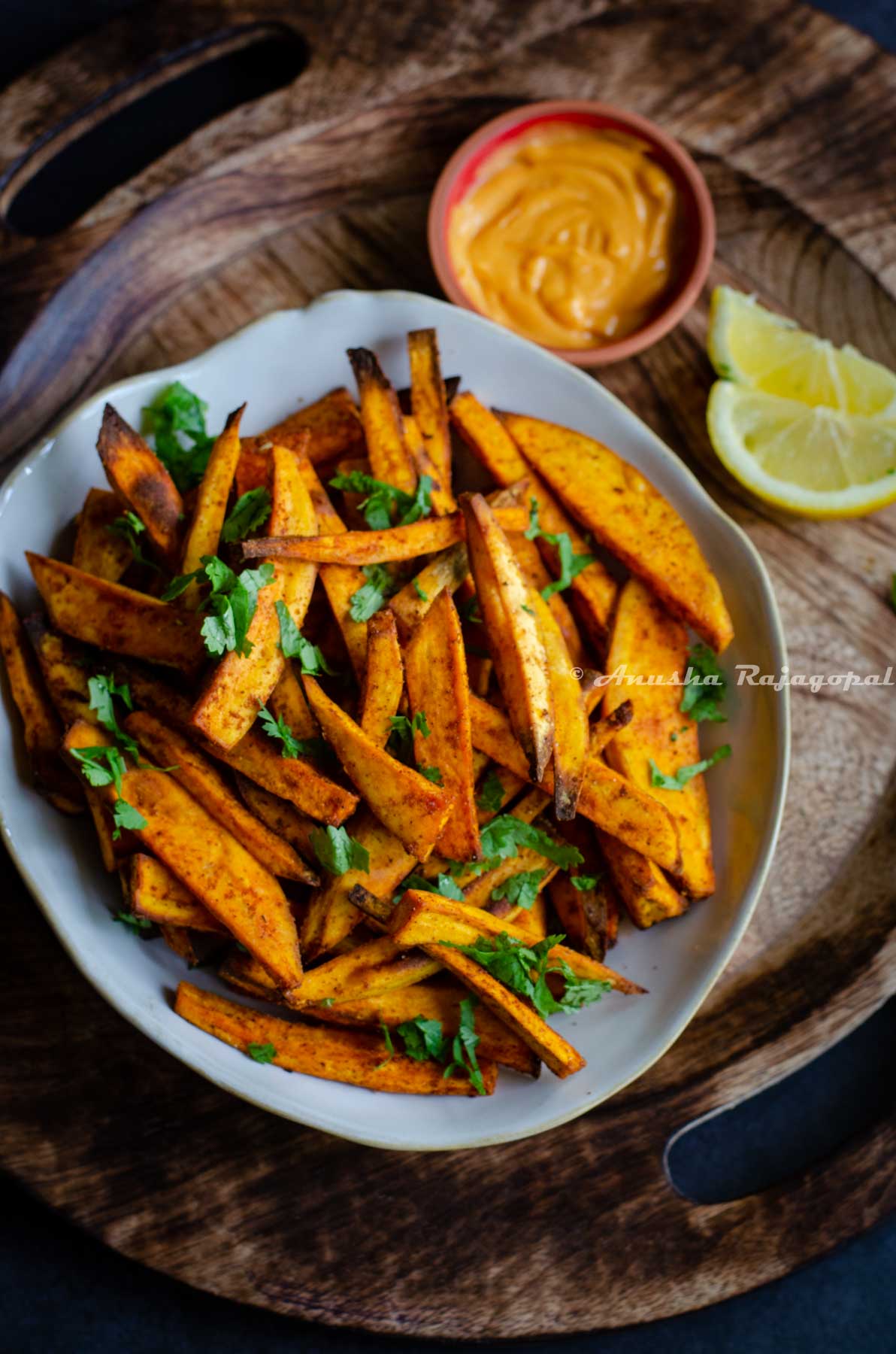 air fried sweet potato chips served in a beige irregular rimmed shallow bowl with spicy dip and lemon wedges