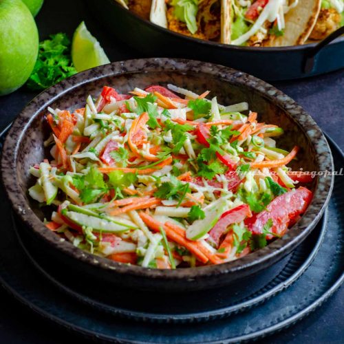 mayo free taco slaw served in a black bowl along side tacos. slaw made with green apples.