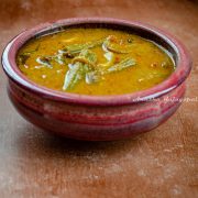 kara kulambu, a tangy gravy with eggplants and moringa served in a rustic red bowl placed over a brown backdrop