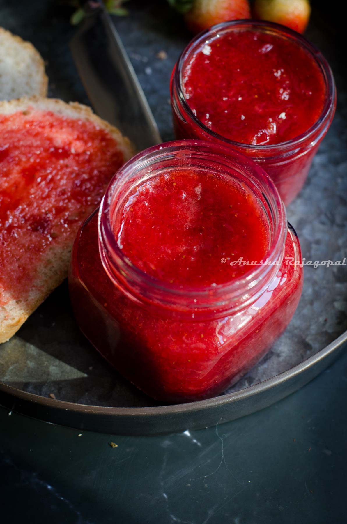 Easy 4 ingredient instant pot strawberry jam in small glass jars. A slice of bread smeared with jam on top by the side. Some strawberries at the back. A bread knife beside the jars.