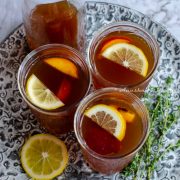 Three glasses of Iced peach oolong tea served with lemon wedges and peach slices as garnish.
