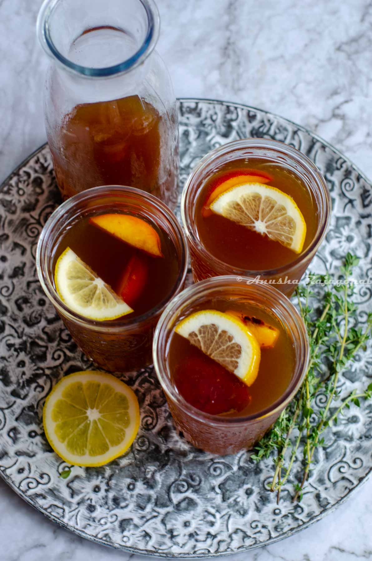 Three glasses of Iced peach oolong tea served with lemon wedges and peach slices as garnish.