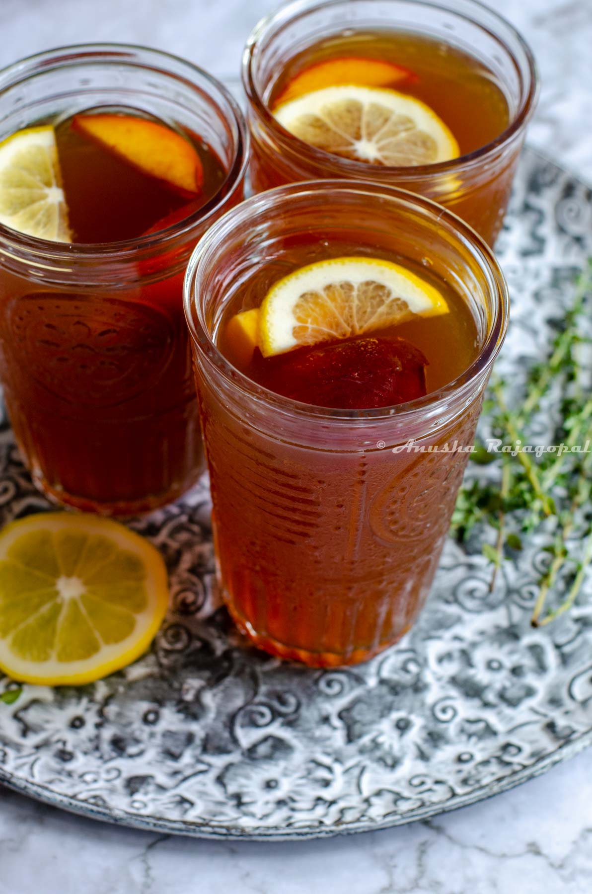 Iced peach oolong tea served in glasses with lemon wedges on the top. By the side, thyme sprigs 