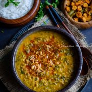 Kale dal served with a tempering of fried garlic and red paprika on top. The bowl of dal is placed over a burlap map. Rice and veggies served in wooden bowls by the side.