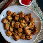 air fried tofu served in an asymmetric rimmed bowl with red chili sauce. chopsticks by the bowl