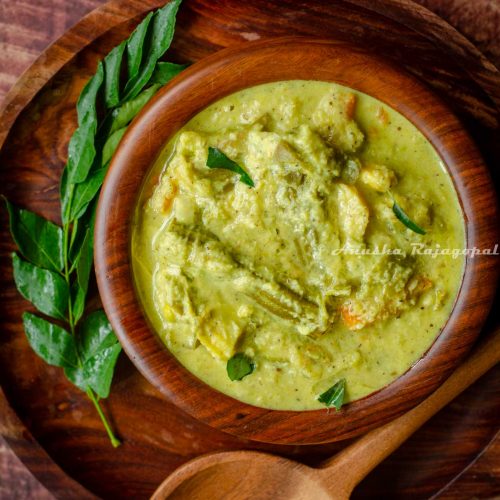 Kerala aviyal served in a wooden bowl placed over a wooden platter. A serving ladle and a sprig of curry leaves placed around the bowl.