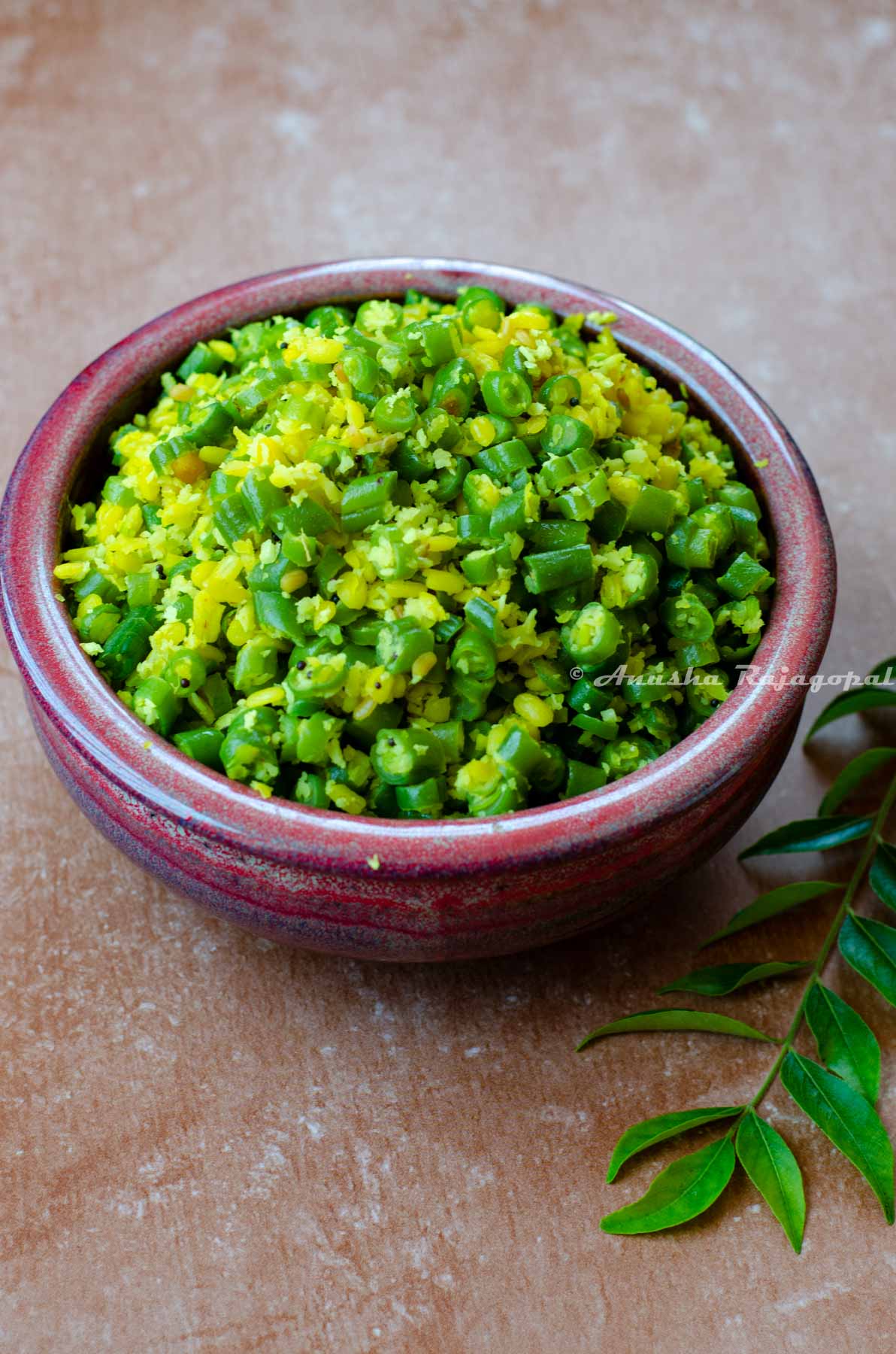 green beans poriyal served in a reddish brown bowl with curry leaves by the side