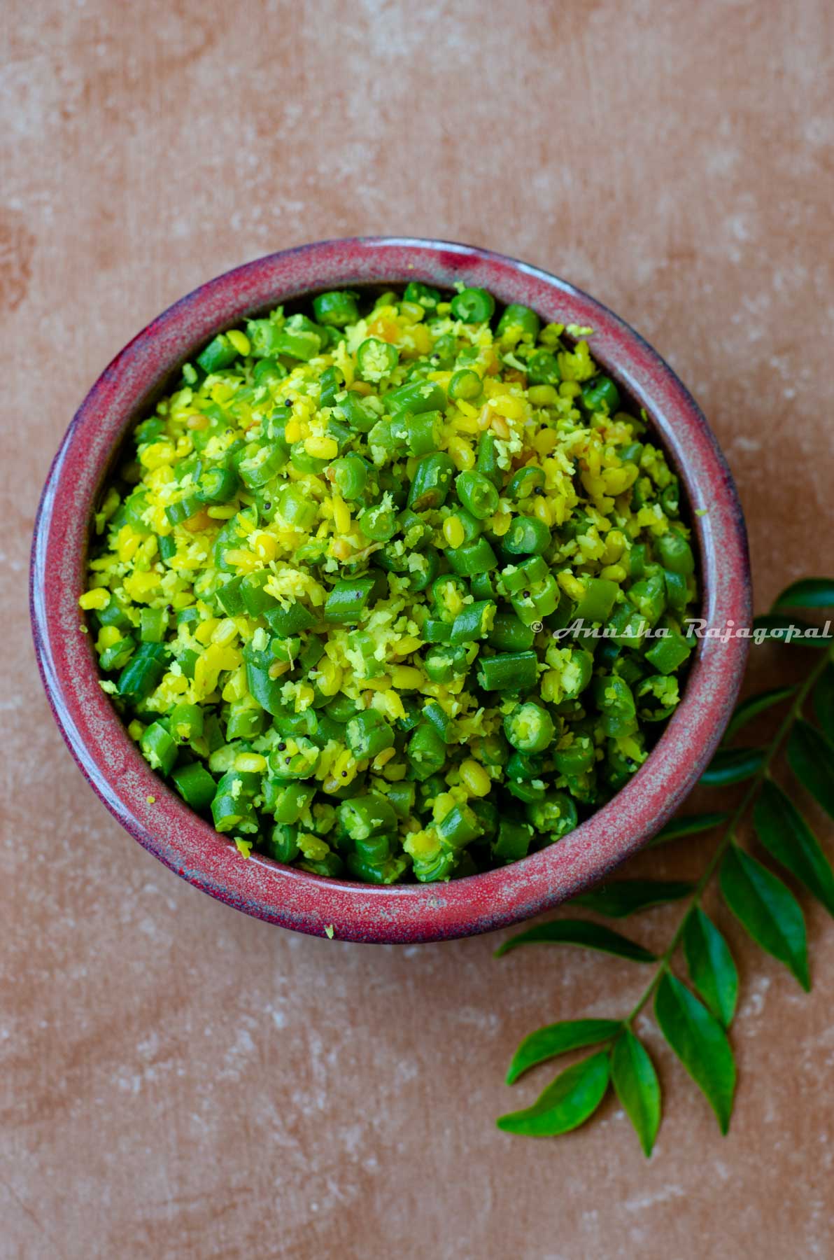 green beans poriyal served in a reddish brown bowl with curry leaves by the side