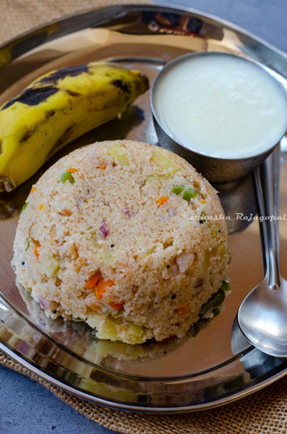broken wheat upma with banana and yogurt in a bowl. A spoon lies by the side.