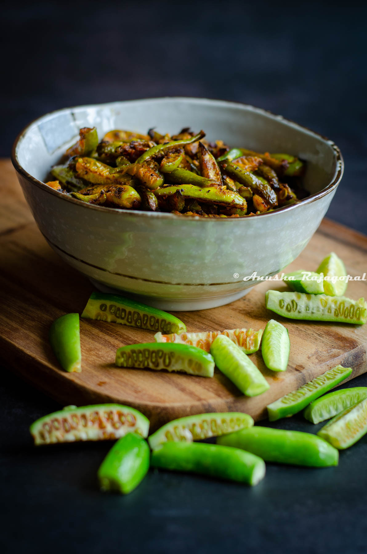 Kovakkai fry served in a beige ceramic bowl placed over a wooden board. Sliced kovakkai scattered around the bowl on the board