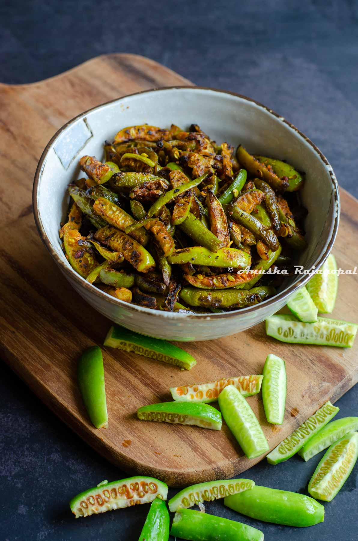 Kovakkai fry served in a beige ceramic bowl placed over a wooden board. Sliced kovakkai scattered around the bowl on the board