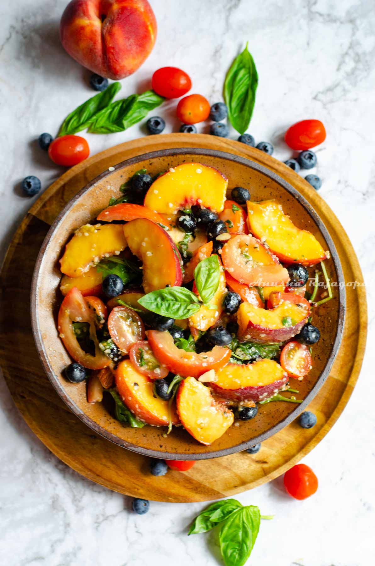 vegan peach salad with summer fruit served in Khaki brown shallow bowl placed over a wooden plate. Fruits scattered around the plate.
