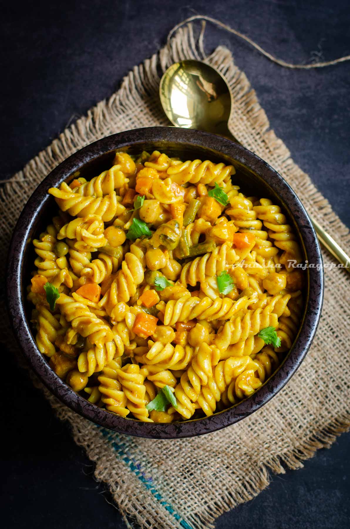 Hearty curry pasta served in a black bowl with a golden spoon.