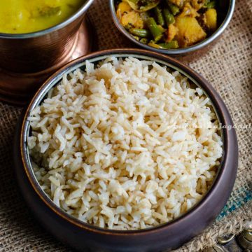 A bowl of brown basmati rice, some toor dal and a beans potato vegetable curry presented together.