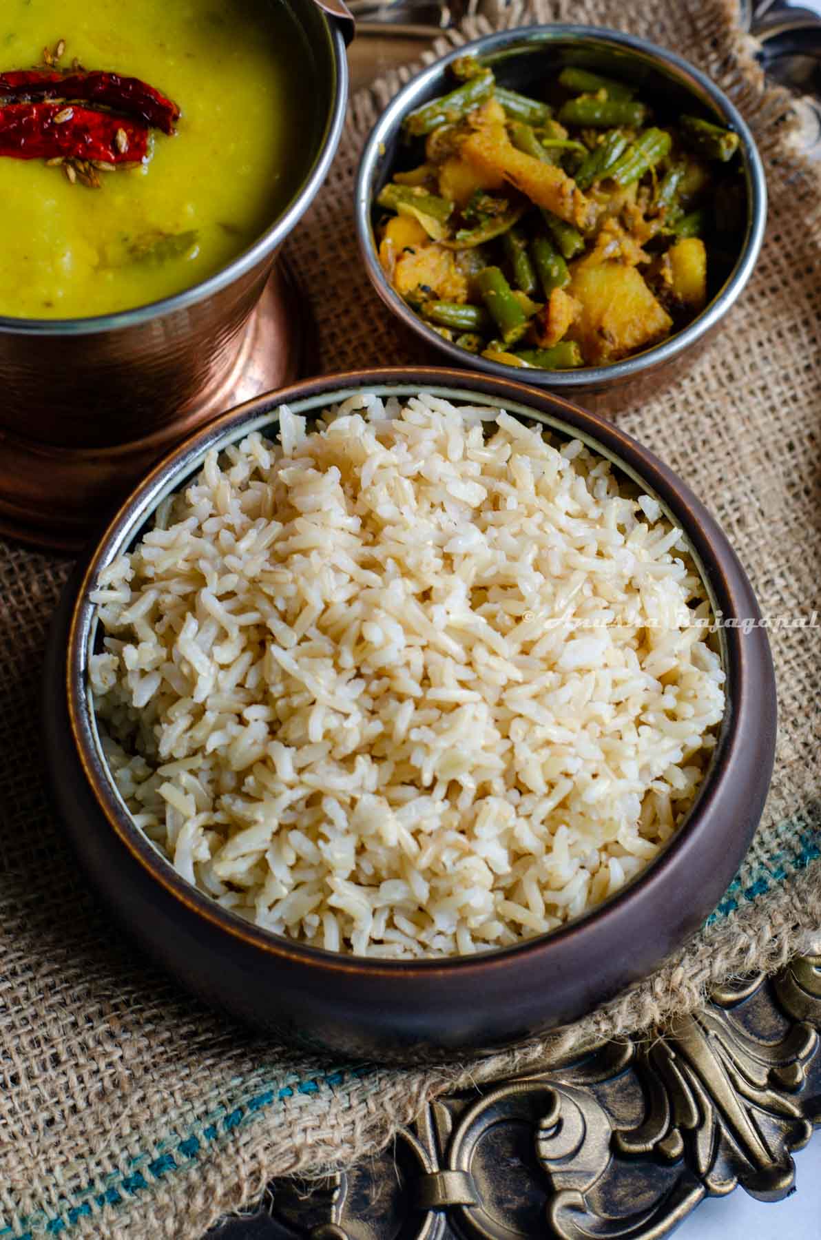 A bowl of brown basmati rice, some toor dal and a beans potato vegetable curry presented together.